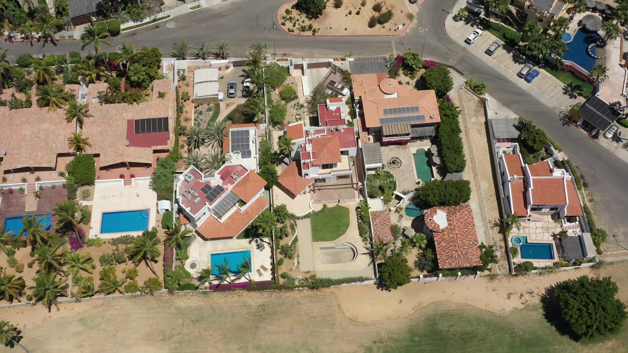Overhead view of homes, pools, palms, roads, and dry landscaped lots.