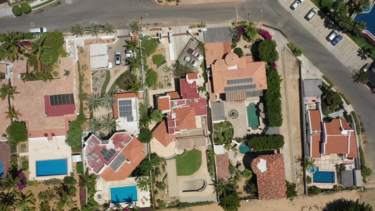 Top-down neighborhood view with pools, roofs, and a road junction.