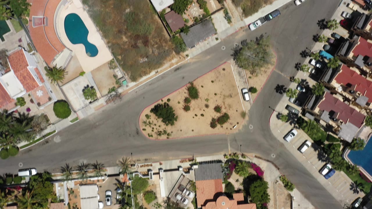Top view of a residential intersection, landscaped island, villas, and parked vehicles.