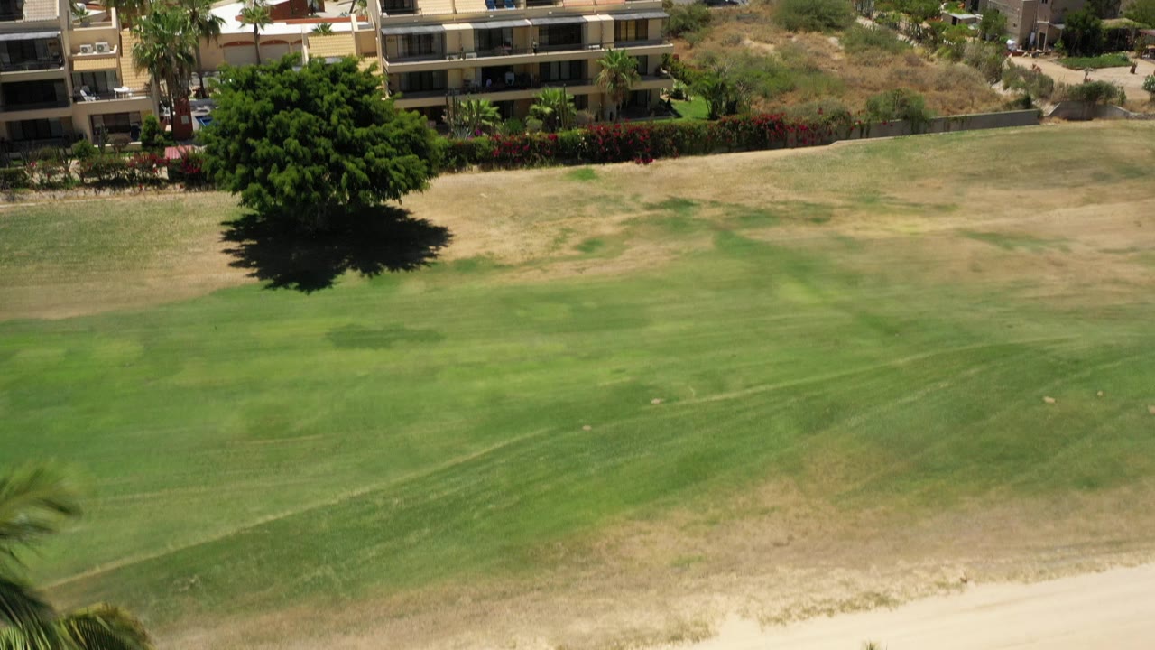 Aerial view across field toward apartments and dry hillside.
