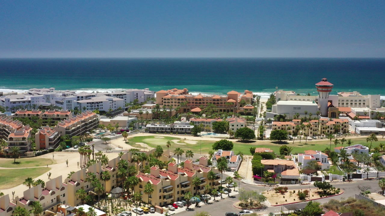 Aerial view of coastal buildings, landscaped grounds, roads, and blue ocean.