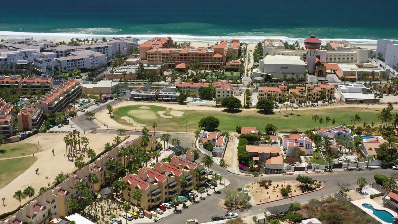 Aerial coastal view with ocean, beachfront blocks, red roofs, roads, and palms.