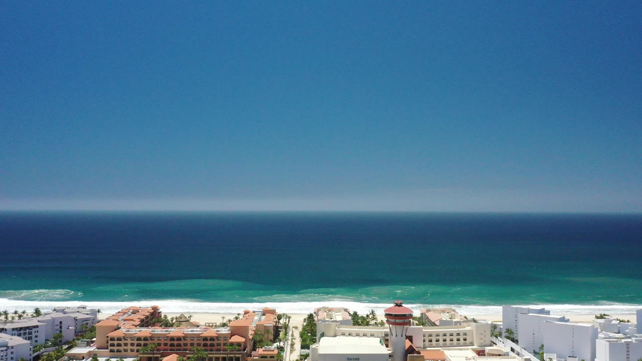 Wide coastal view with blue sky, ocean, beach, and resort buildings.