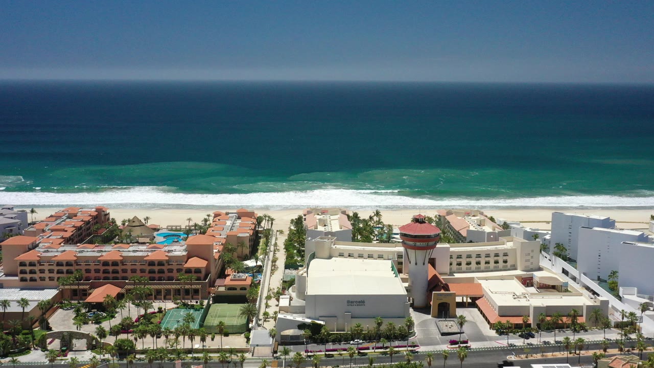 Aerial view of beachfront resort buildings beside teal ocean surf.