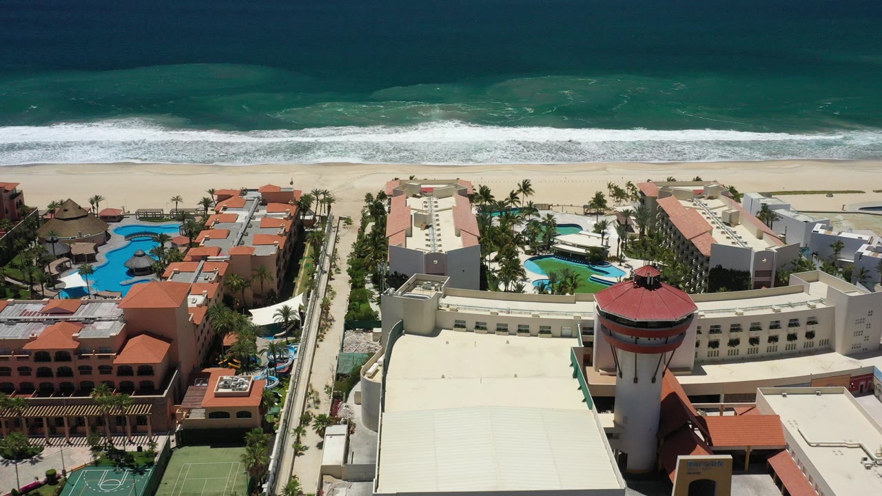 Aerial view of resort buildings, pools, beach, and ocean surf.