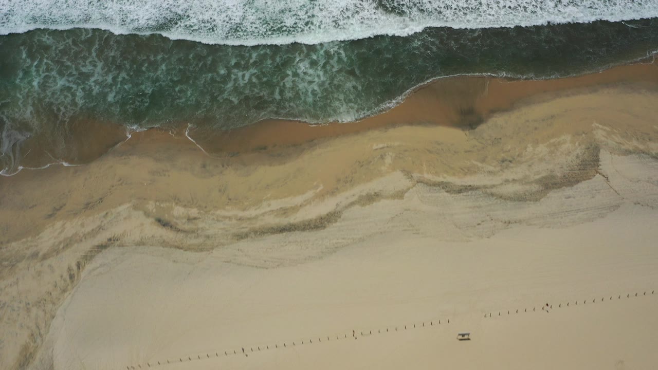 Overhead surf and tan beach with foamy water at the shoreline.