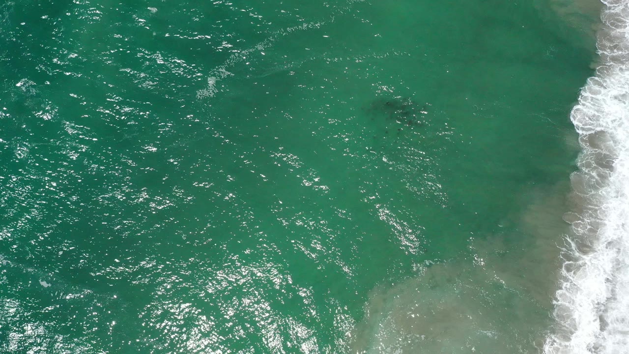 Turquoise sea with shallow sand color and foamy surf at the far right.