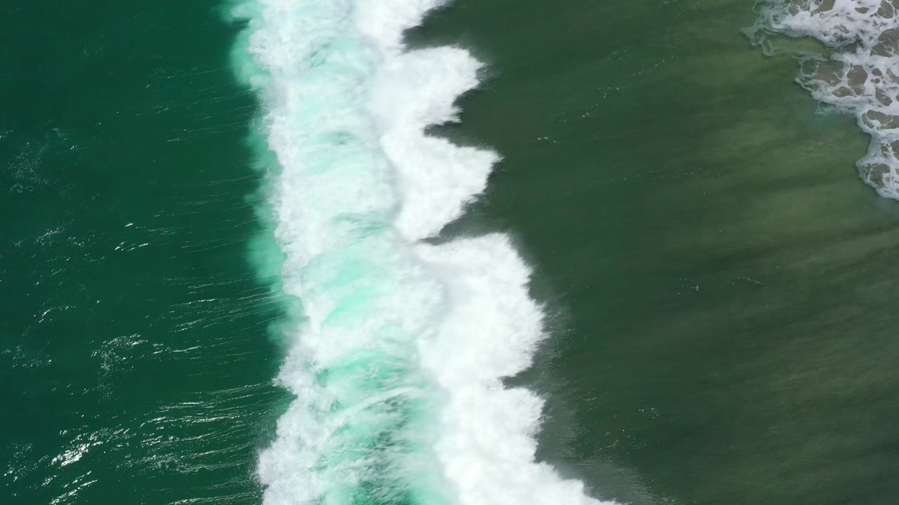 Foamy ocean wave spreads across green water near shallow sand.