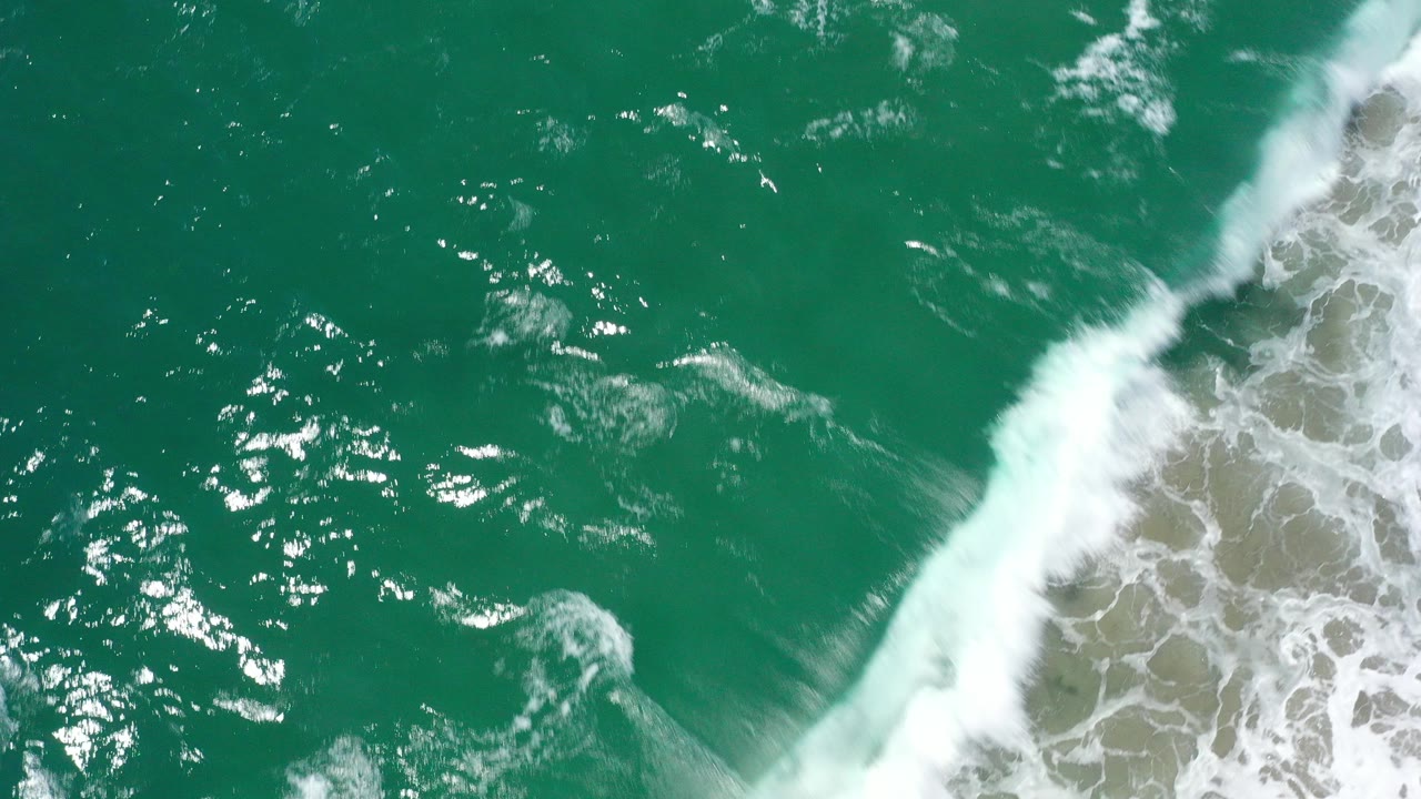 Downward aerial view of green ocean water in San Jose Del Cabo, Mexico, with a band of white surf and no visible people.