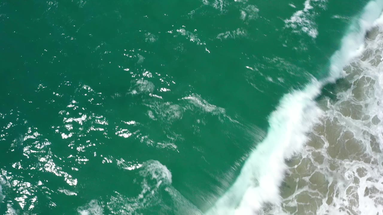 Green sea surface in San Jose Del Cabo, Mexico, with breaking white foam pushed toward the right edge and no visible people.