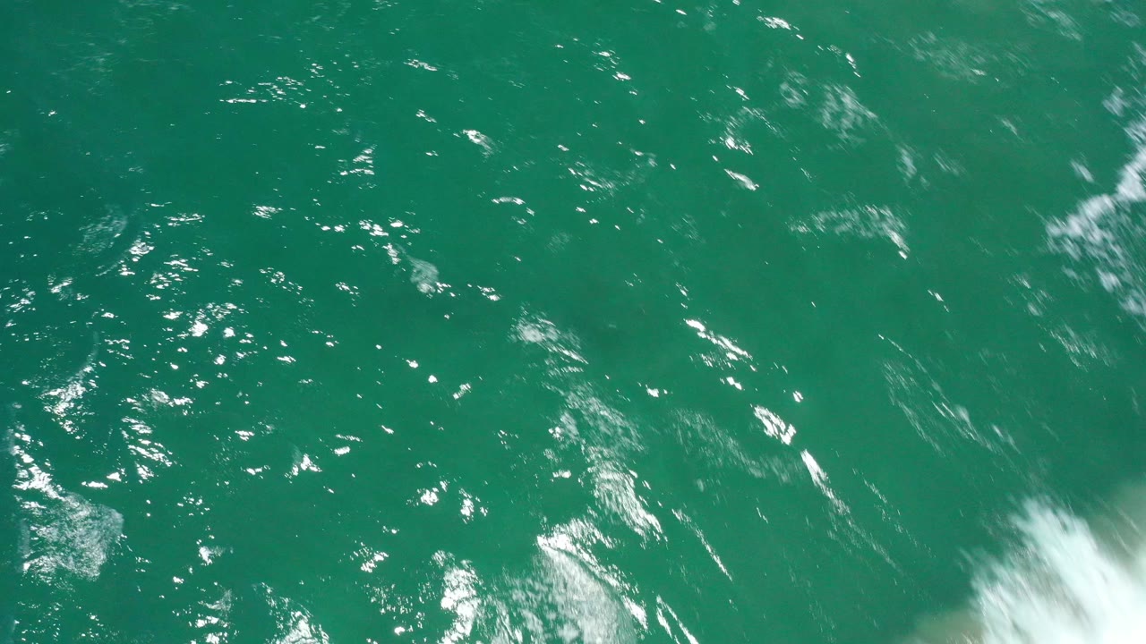 Sunlit green ocean with a partial white wave at the lower right.