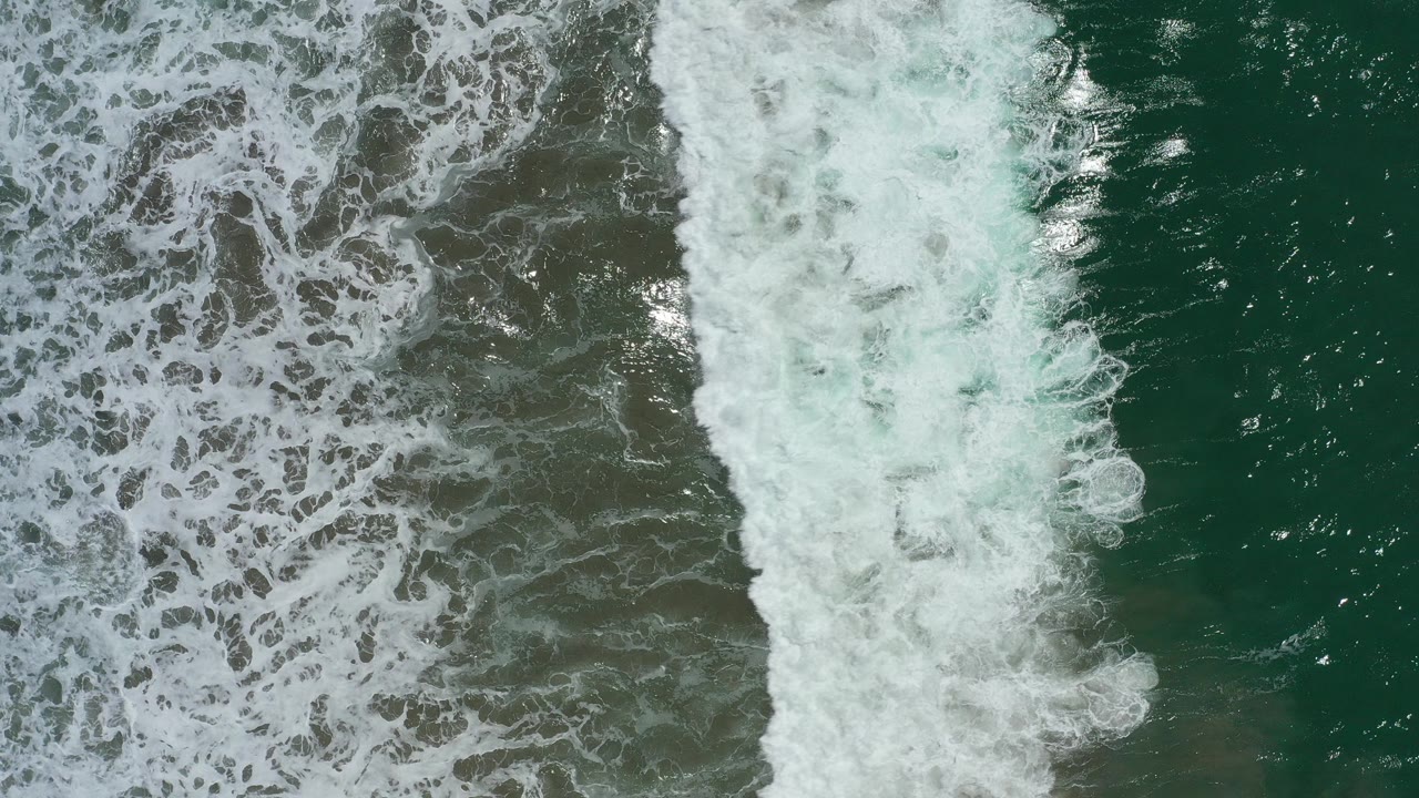 Top-down surf foam over green water and dark wet sand.