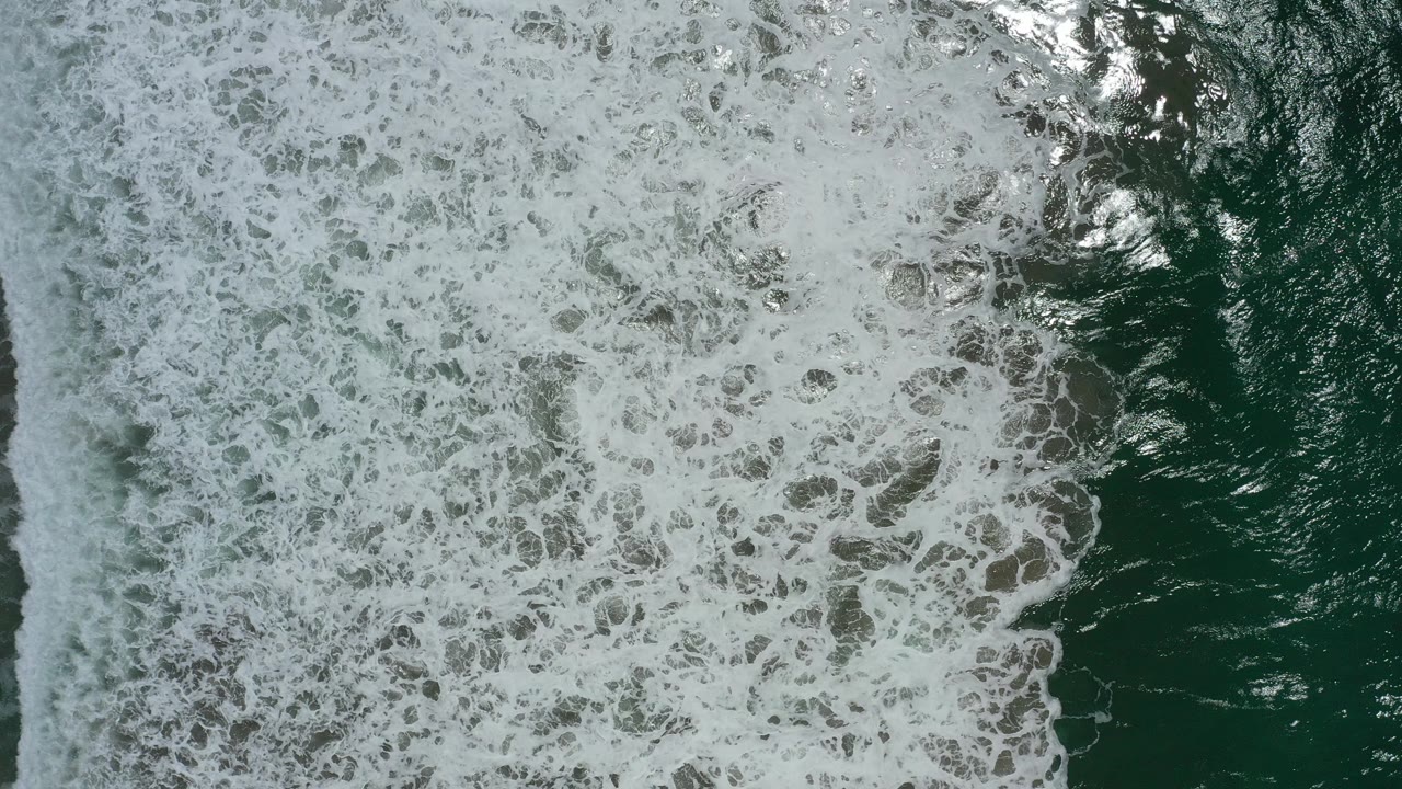 Overhead dark green ocean water covered by white surf foam.
