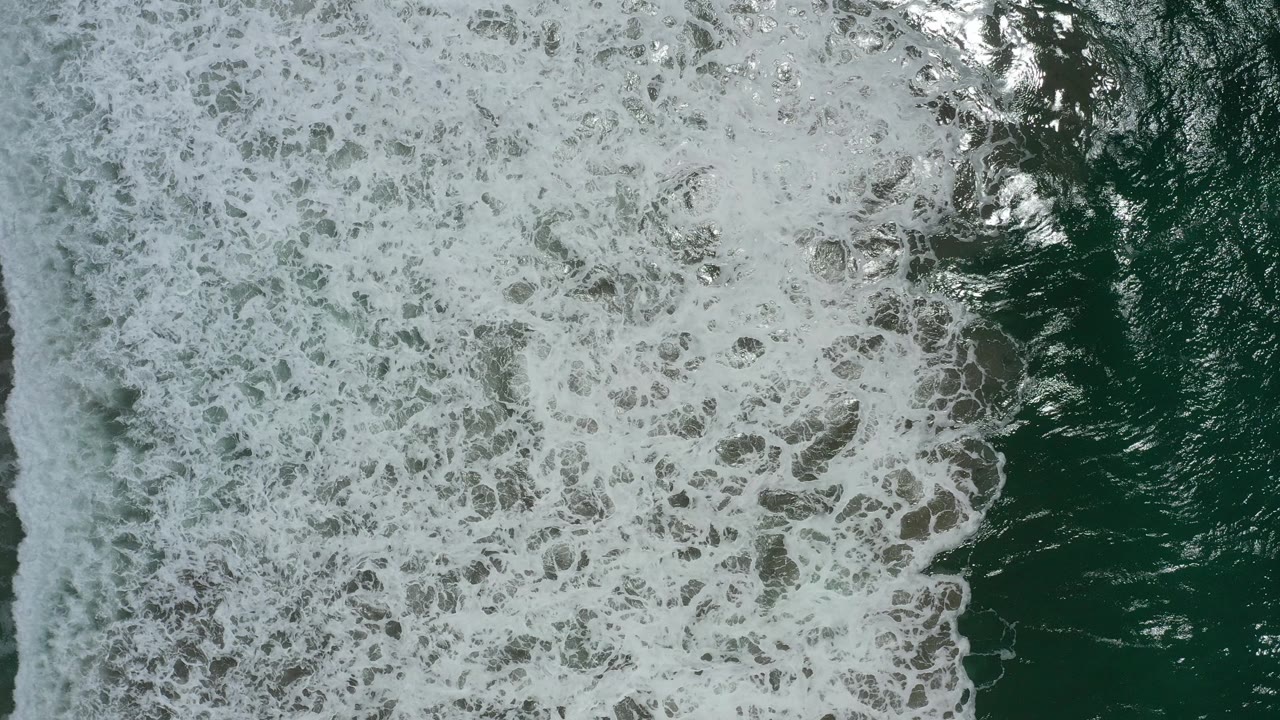 Aerial-style overhead frame of foamy waves advancing across dark green water in San Jose del Cabo, Mexico, with no visible people.