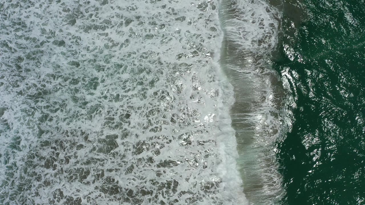 A vertical band of white surf separates foamy water from darker green ocean in San Jose del Cabo, Mexico, with no visible people.