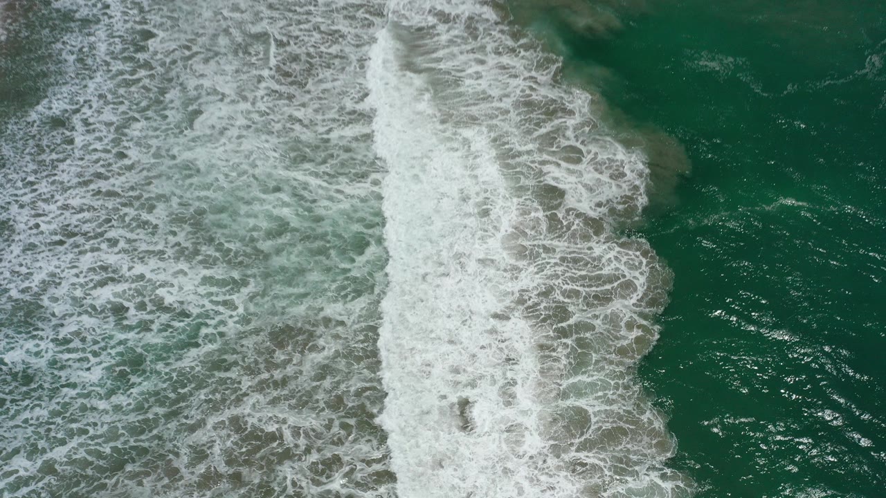 Overhead view of green-blue ocean in San Jose del Cabo with a wide band of white surf crossing the frame and no visible people.