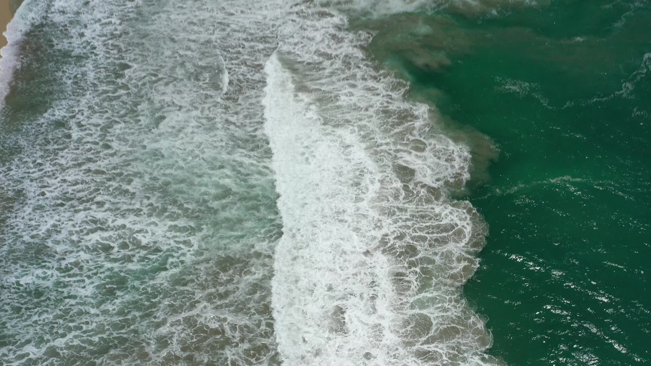White surf breaks along the right side of an overhead San Jose del Cabo ocean frame, leaving darker green water visible to the far right and no visible people.