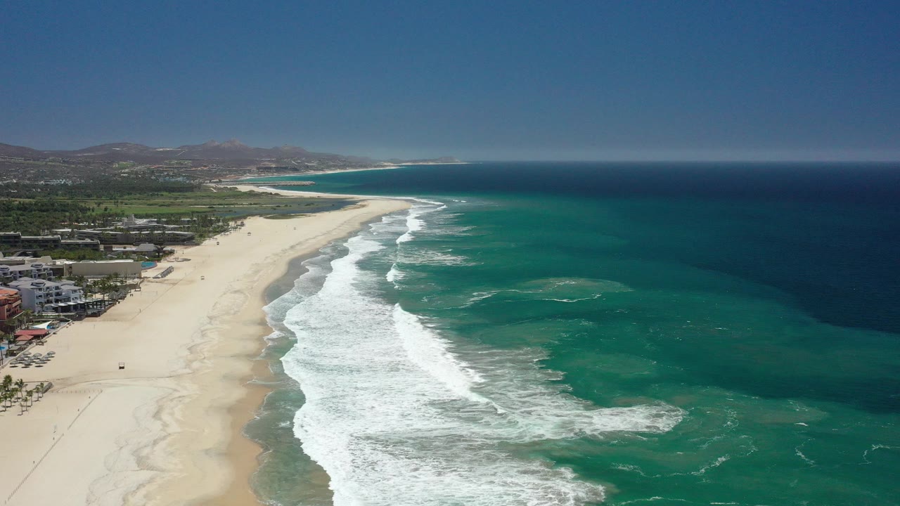 Aerial view of a sandy beach, teal ocean, and white surf.