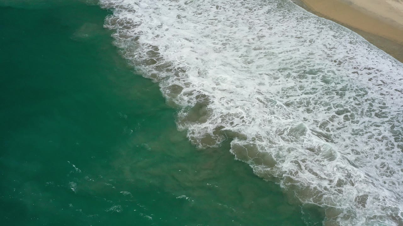 Diagonal surf line over deep green coastal water.