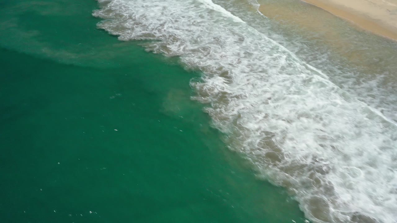 Aerial shoreline with surf foam and beach at the top edge.