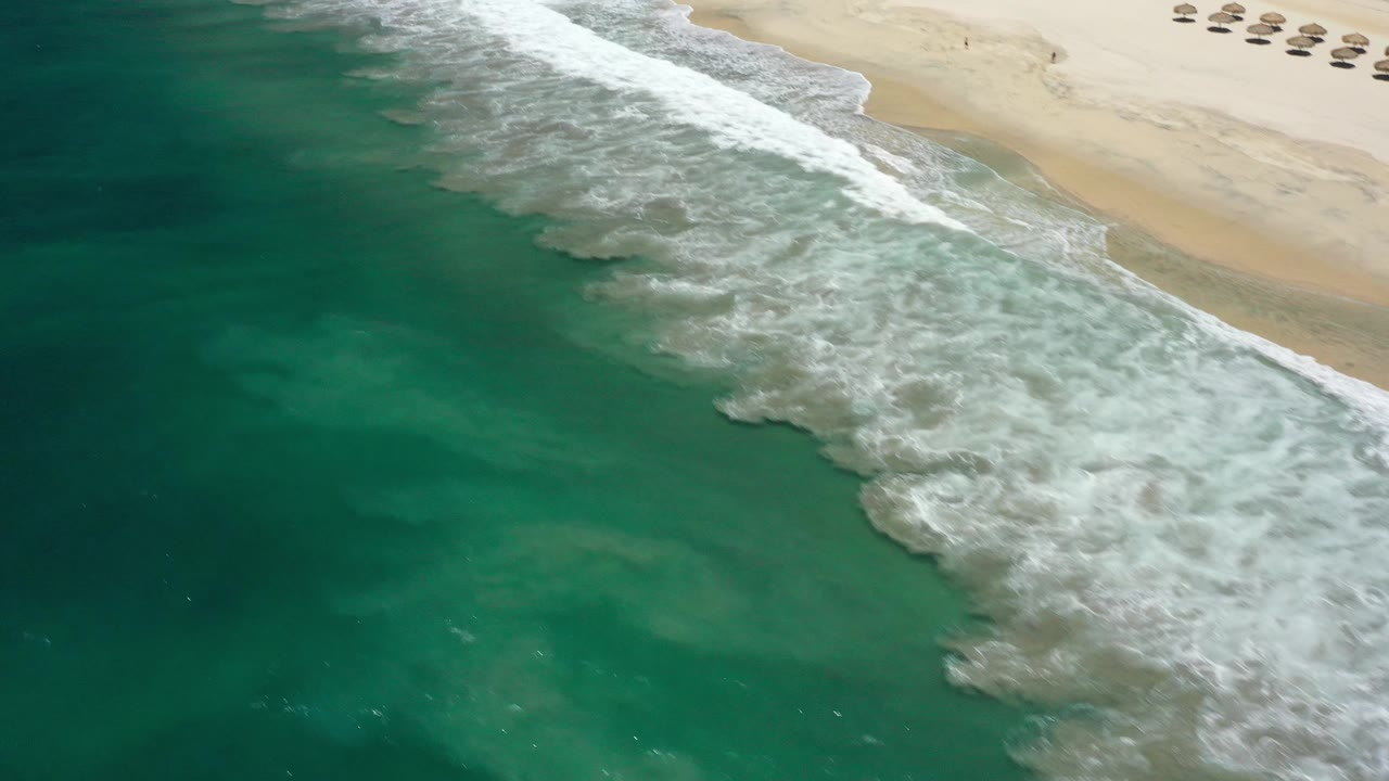 Wide aerial shoreline with rolling surf and green ocean water.