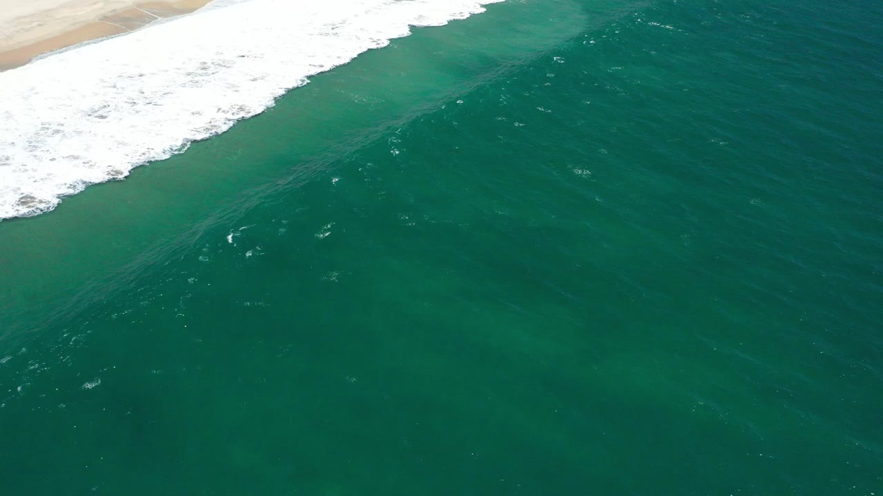 Overhead green ocean with white surf and pale sand at the top edge.