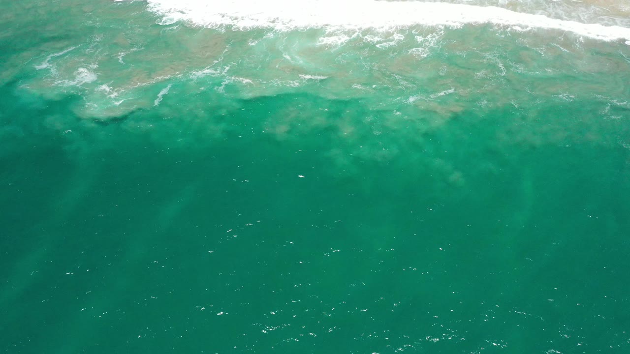 Top-down green-blue ocean in San Jose Del Cabo, Mexico, with foamy water spread across the upper shoreline band and no visible people.