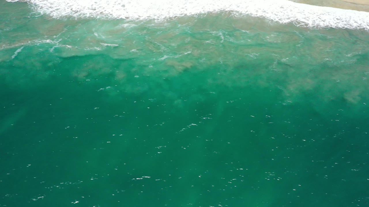 Open turquoise sea with pale surf and sand near the top.