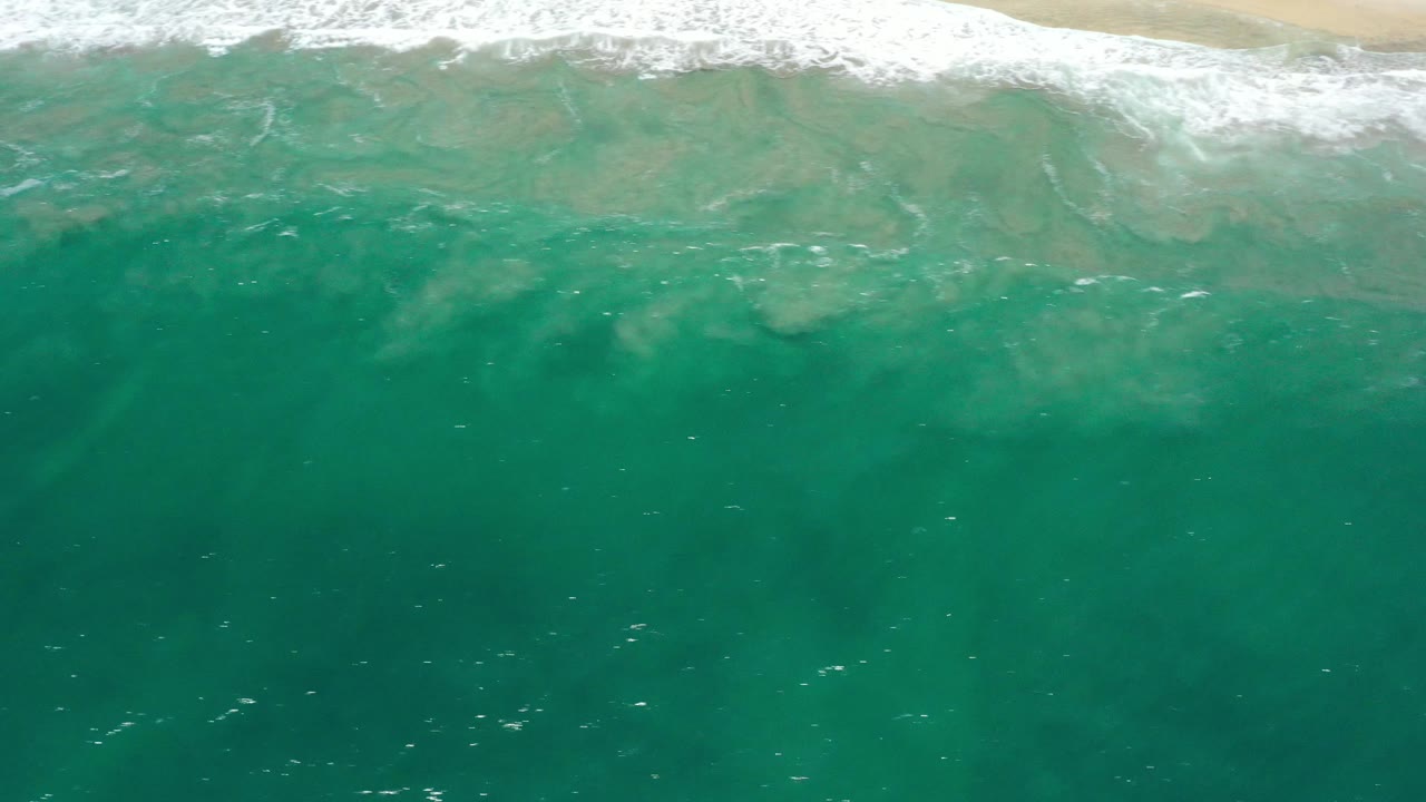 Ocean surface with scattered foam below a sandy shoreline.
