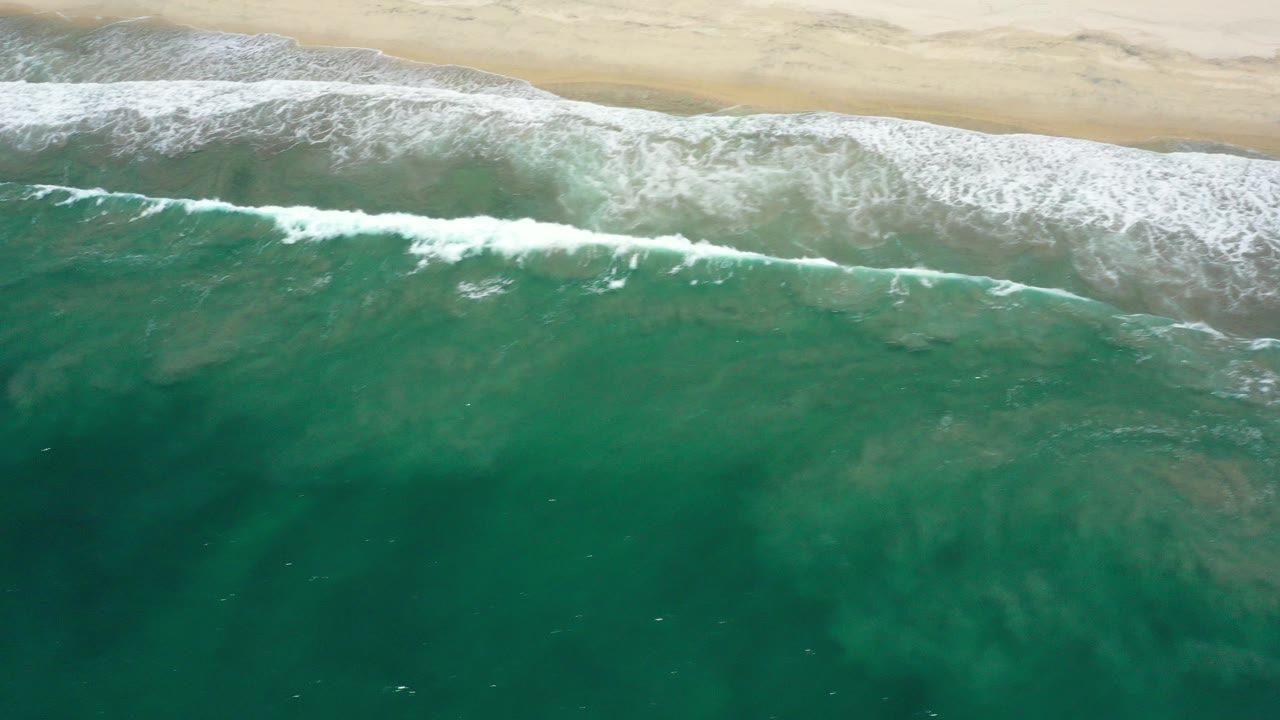 Aerial view of teal ocean waves meeting a sandy beach.