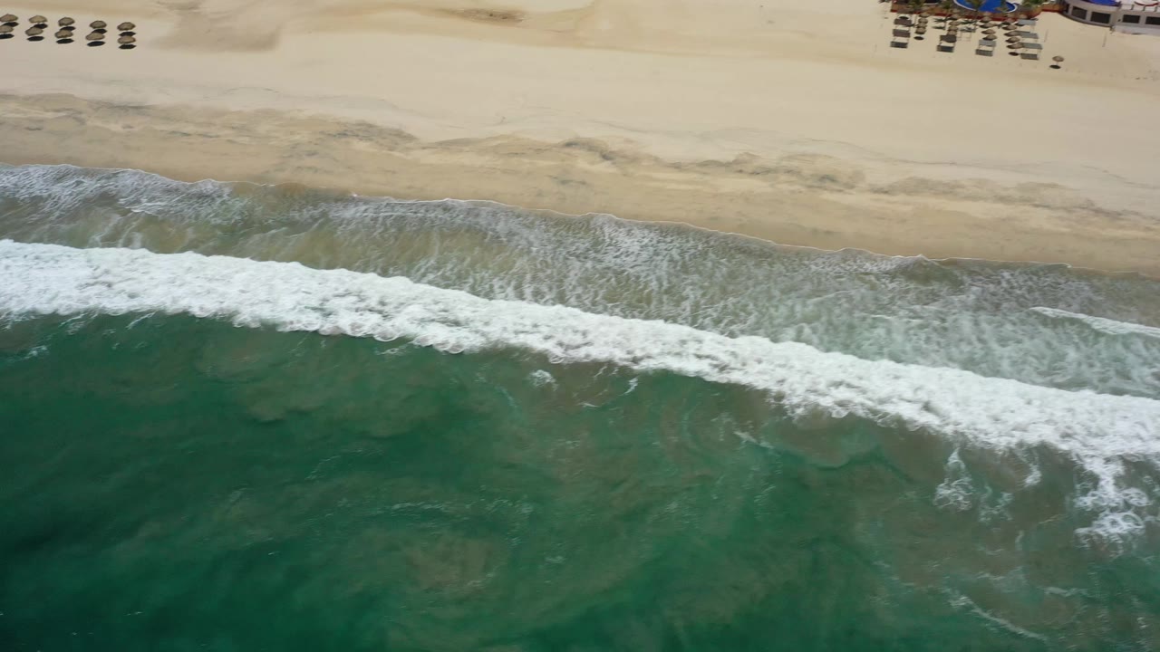 Aerial shoreline with white wave foam and empty sand.