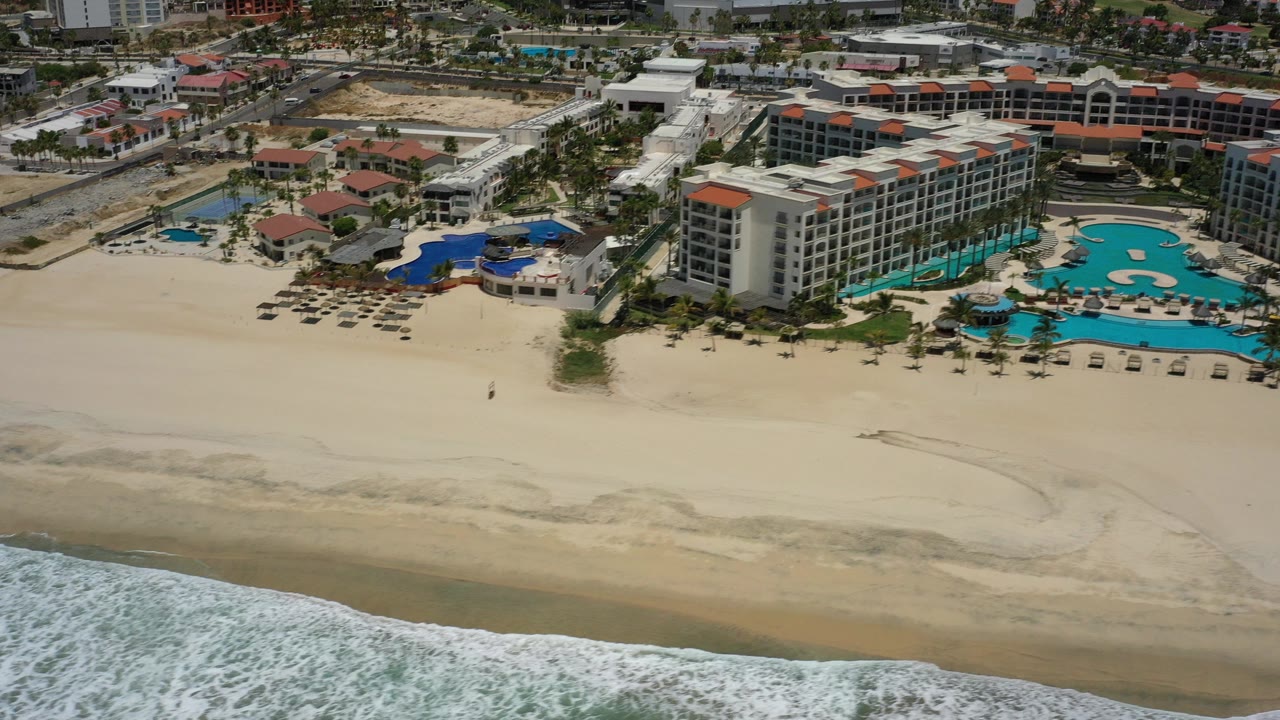 Aerial view of a beachfront resort beside a wide sandy beach and surf.