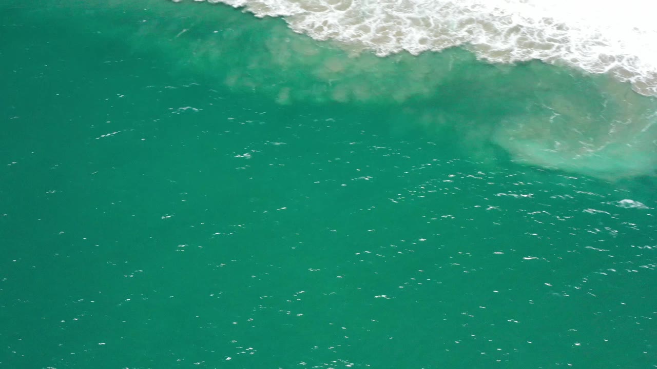 A slightly shifted overhead frame shows the whitewater band across the upper edge above green-blue ocean in San Jose del Cabo, with no visible people.