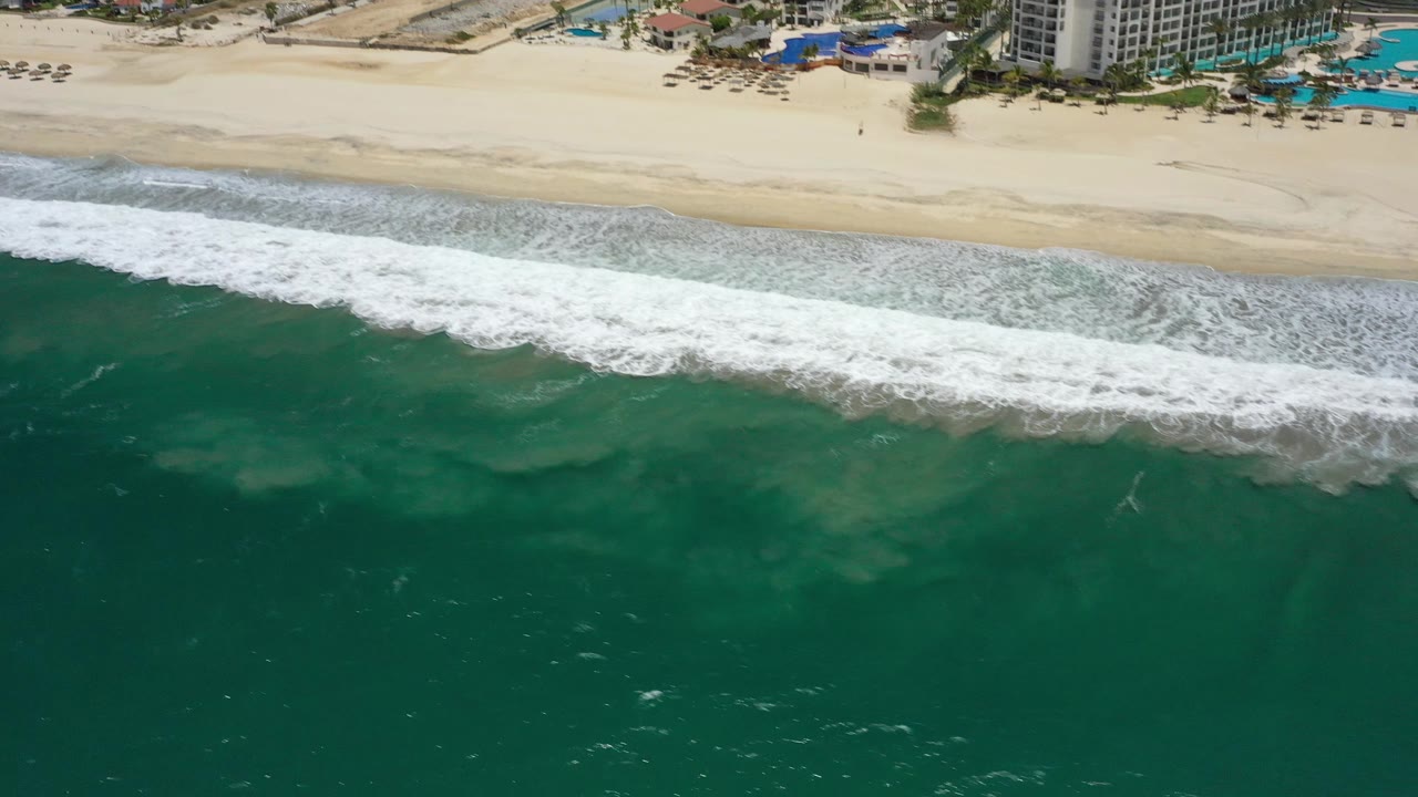 Oblique aerial view of surf, sand, pools, and large beachfront buildings.