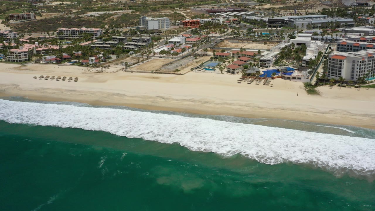 Aerial view of surf, sandy beach, and beachfront buildings.