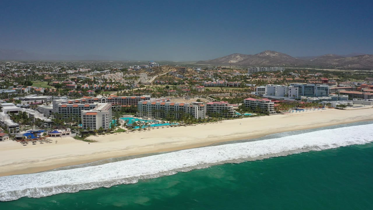 High coastal view of a beach resort area with ocean foreground and dry hills behind the city.