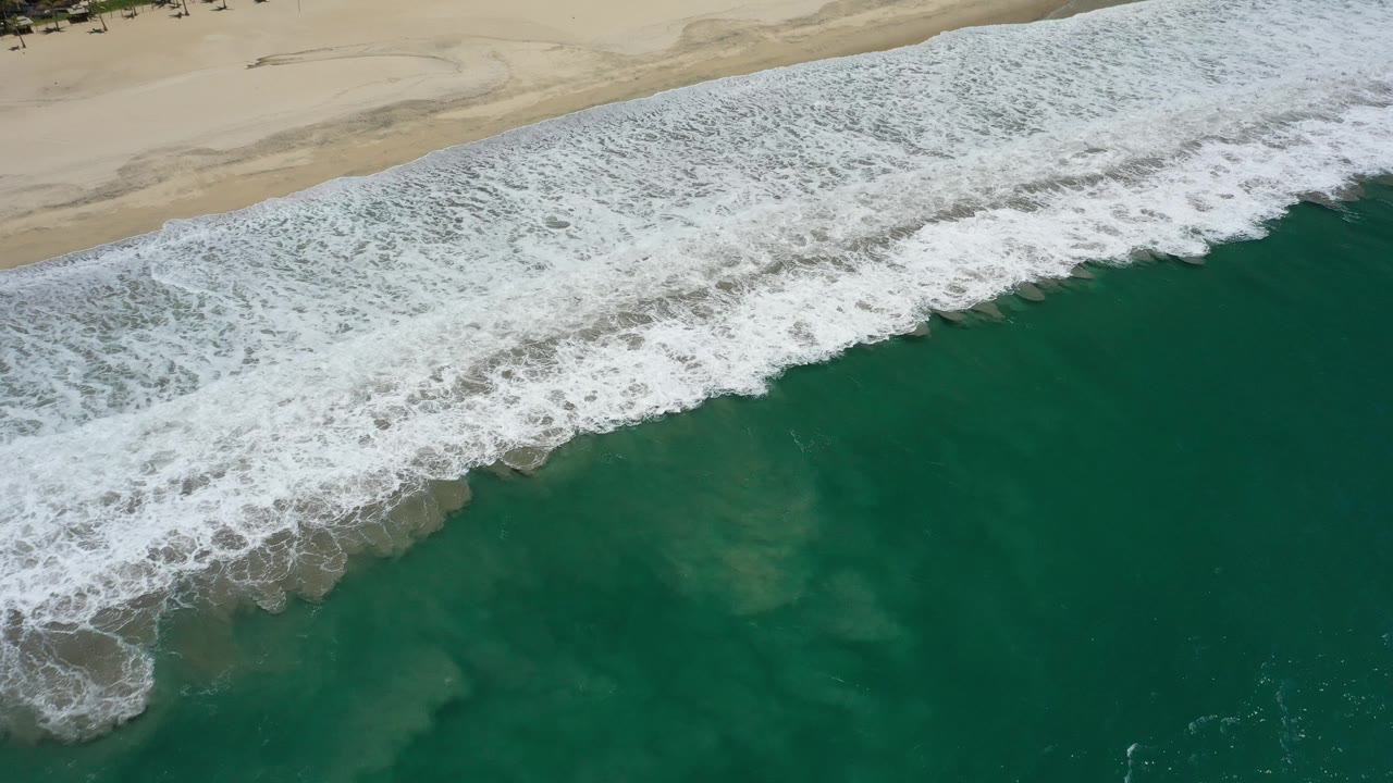 Foamy wave break crossing a dark green shoreline