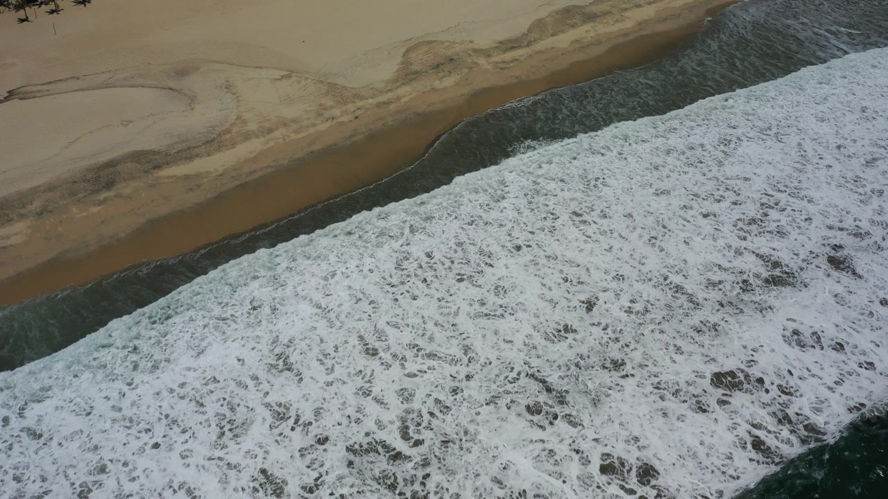Overhead view of foamy surf pushing diagonally across wet sand on a San Jose del Cabo beach, with no clearly visible people in this frame.