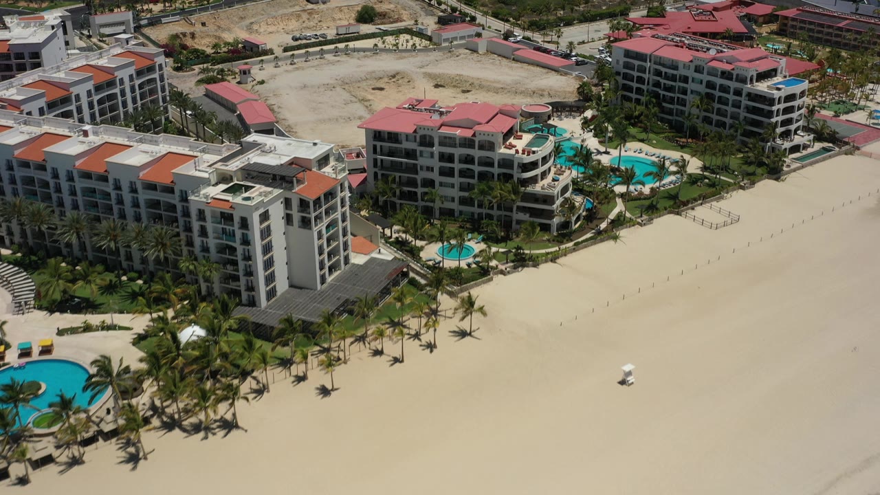 Beachfront hotels with red roofs, palm landscaping, and empty sand below.
