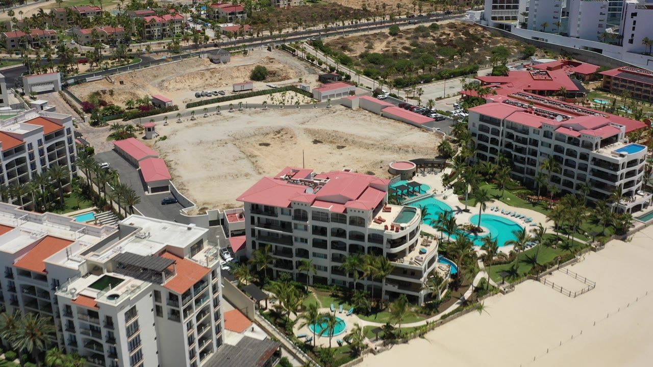 Aerial view of resort buildings, pools, palms, roads, and sandy ground.