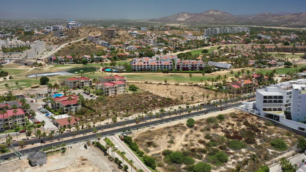 Aerial view over San Jose Del Cabo buildings, roads, golf greens, dry lots, and mountains.