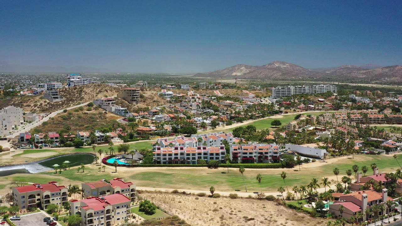 Aerial view of villas, golf greens, pool, desert hills, and distant mountains.