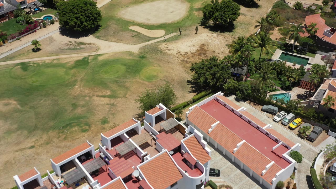 Overhead view with rooftops at the bottom and open green and tan ground above.