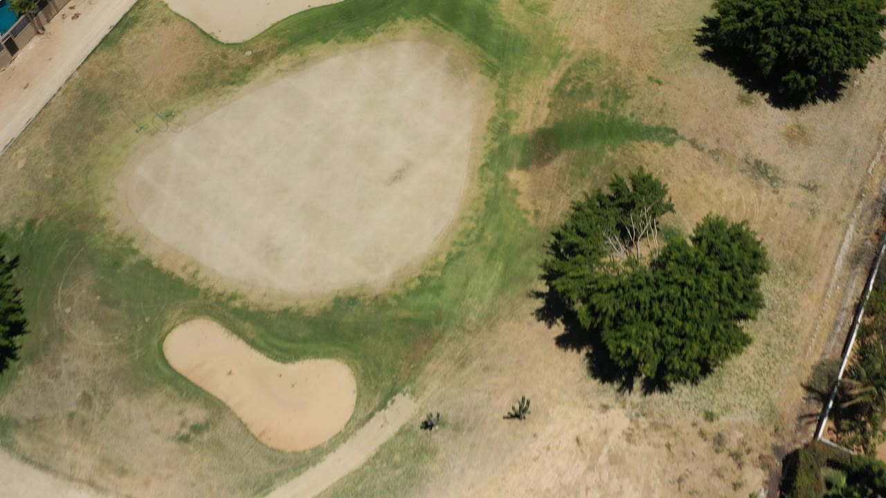 Top-down aerial frame in San Jose del Cabo, Mexico, showing a large pale sand bunker, smaller bunker, green turf edges, dry grass, a path, and no visible people.