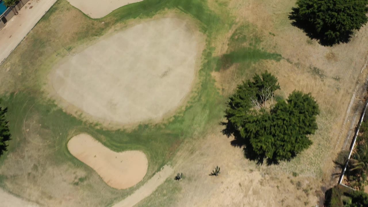 Aerial top view in San Jose del Cabo, Mexico, with the larger bunker near the upper center, a smaller bunker below it, surrounding turf, trees, path, and no visible people.