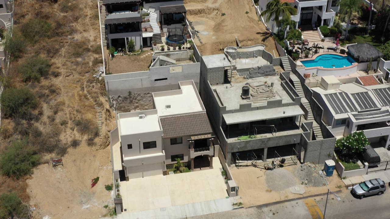 Aerial view of modern hillside homes beside dry brush and a bright blue pool.