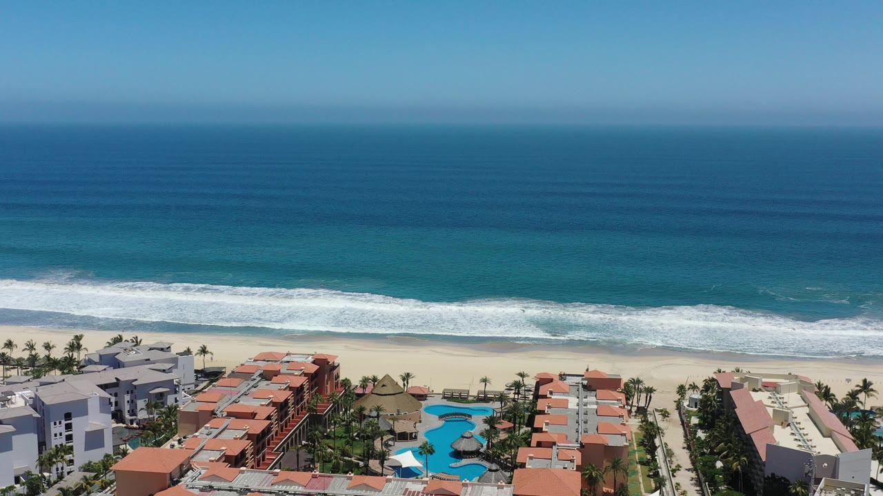 Aerial coastline view with turquoise water, surf, beach, homes, and palms.