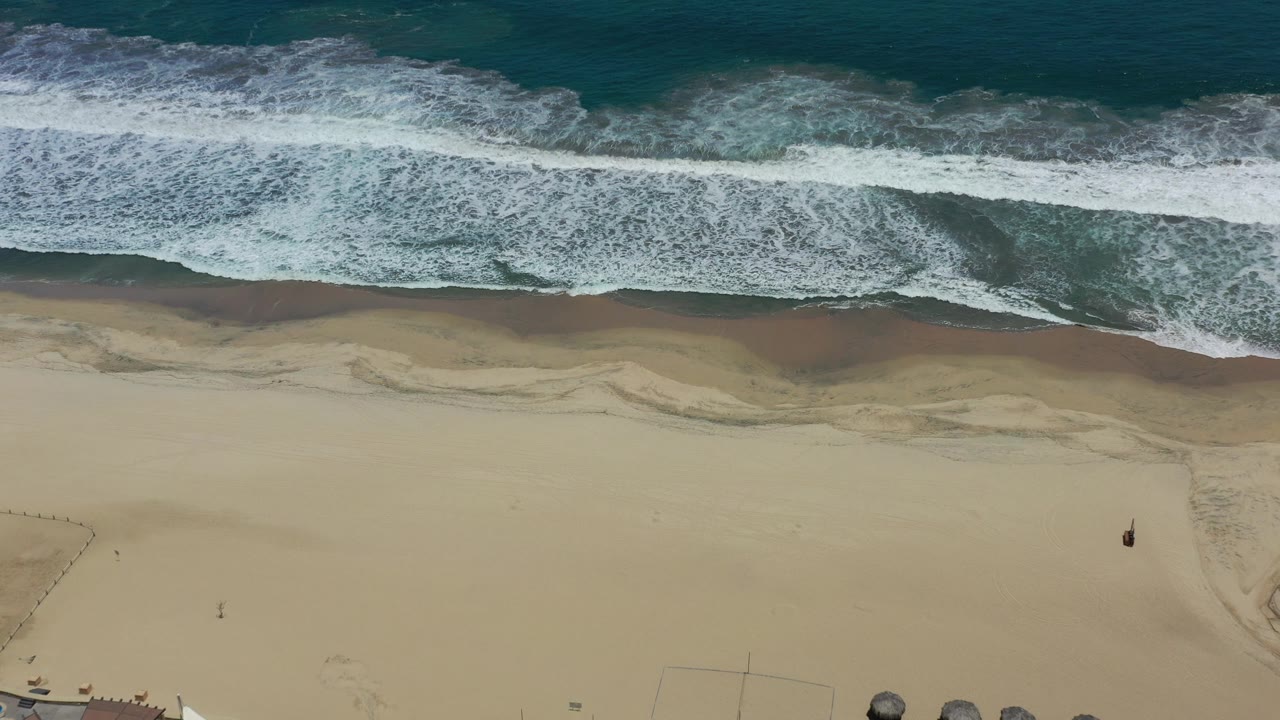 Top-down waves breaking along a wide empty beach.
