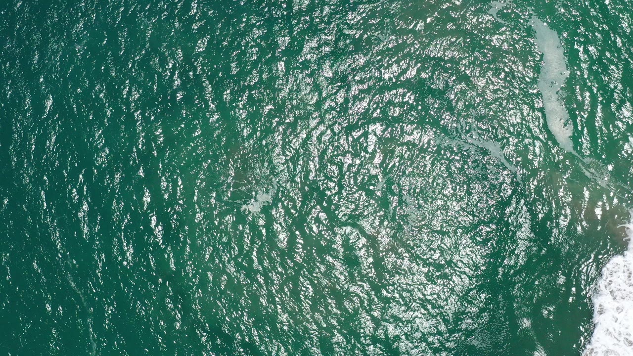 Top-down view of teal ocean water in San Jose del Cabo with bright ripple highlights, a pale foam streak near the right edge, and no visible people.