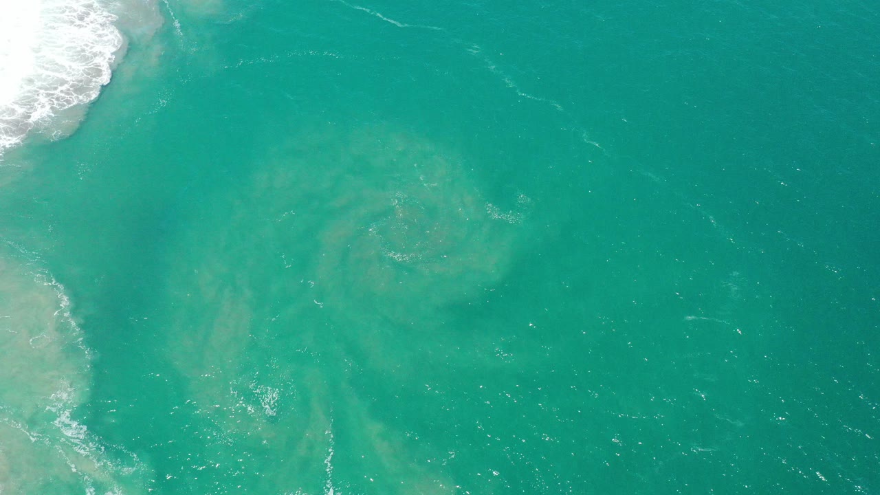 Turquoise ocean with white surf at the left edge and pale sediment below the surface.